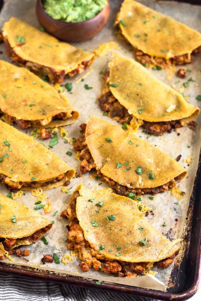 A sheet pan of turkey baked tacos garnished with cilantro. There is also a bowl of guacamole on the sheet pan.