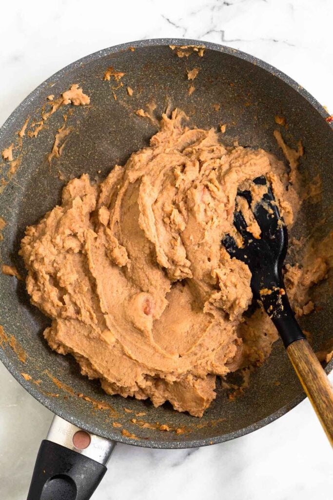 Large skillet filled with warmed up refried beans in it.