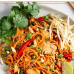 White plate with chicken pad thai made with sweet potato noodles topped with bean sprouts, cilantro, and a lime wedge.