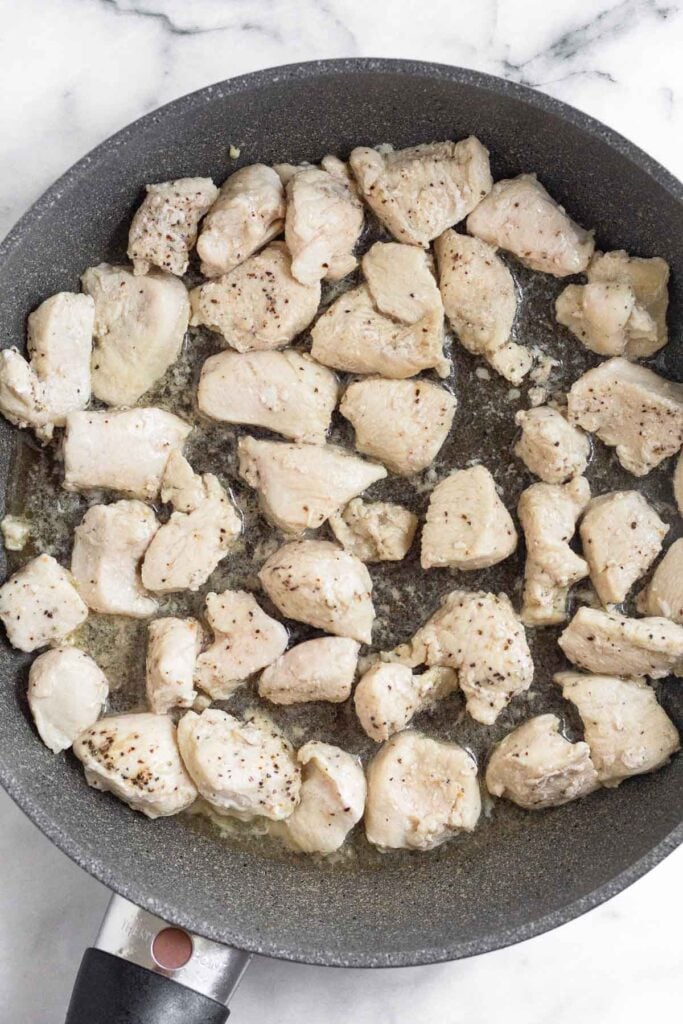 Large skillet filled with bite sized pieces of sautéed chicken.