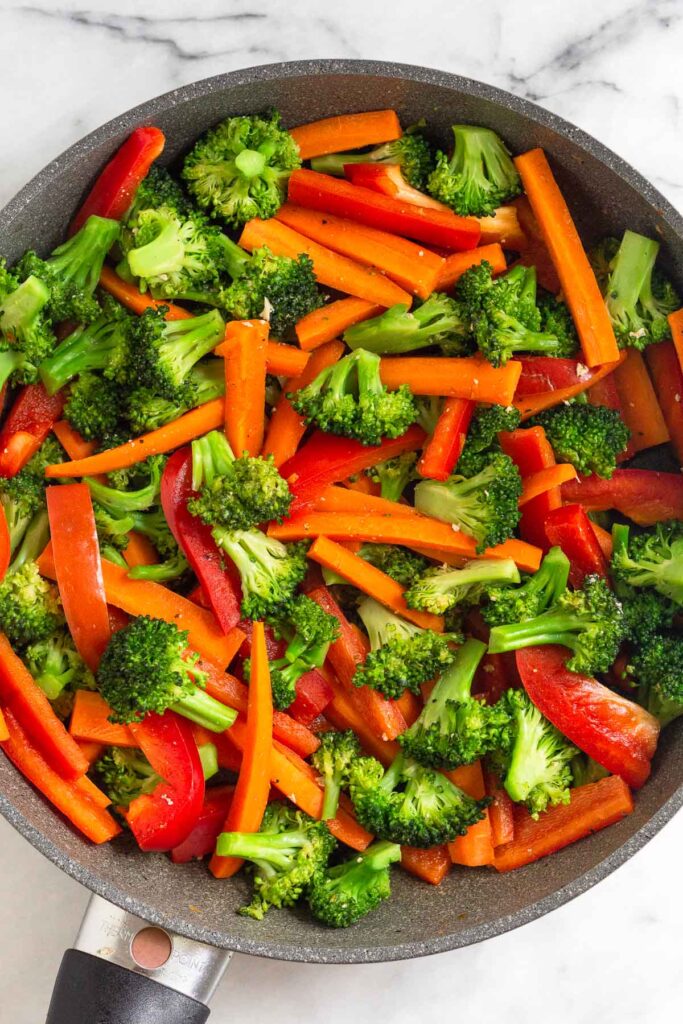 Large skillet filled with sautéed broccoli, carrots, and red bell peppers.