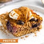 A piece of protein baked oatmeal on a plate topped with yogurt, peanut butter, and cinnamon. Behind it is the pan of the rest of the oatmeal.