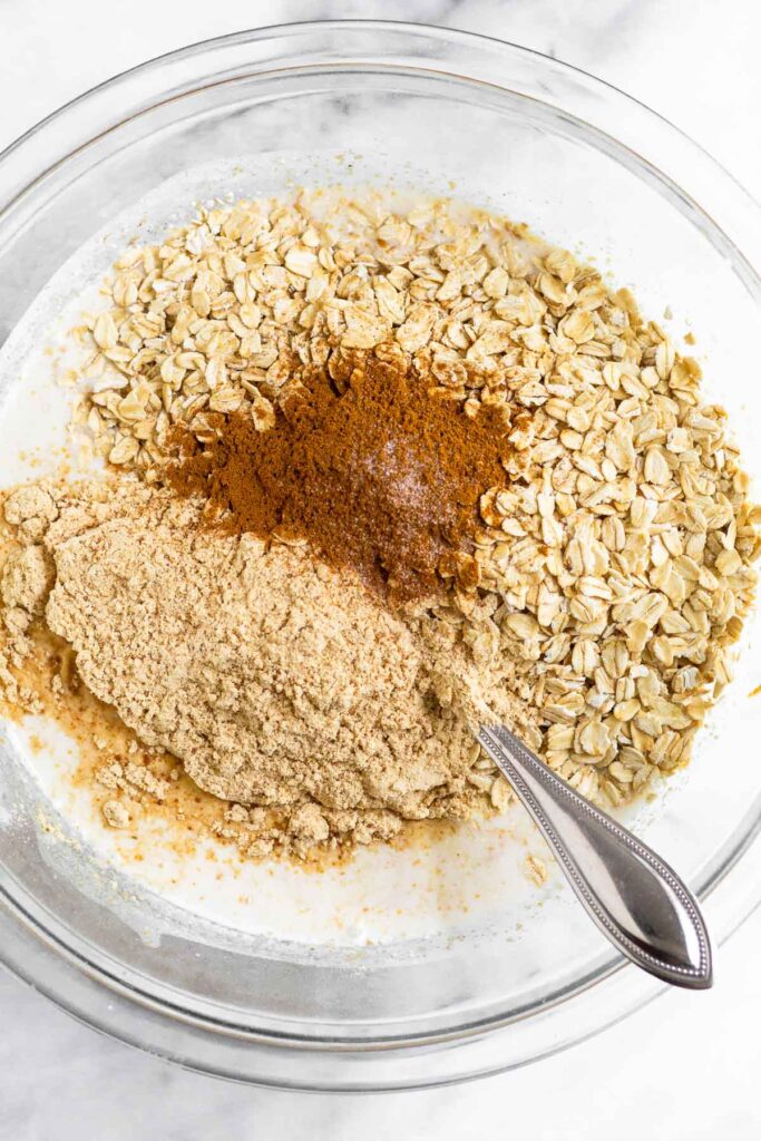 Large bowl with a liquid mixture topped with rolled oats, protein powder, and spices.