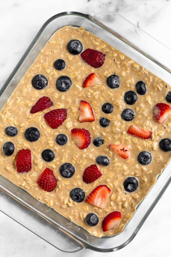 Large baking dish filled with baked oatmeal and sprinkled with berries before it is baked.