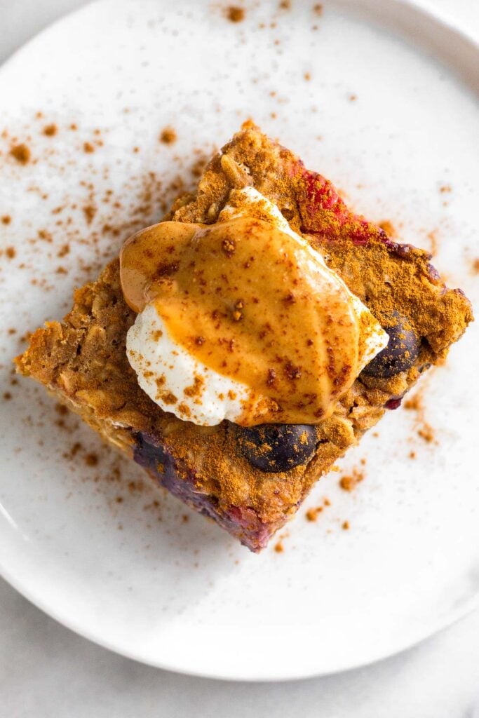 Overhead shot of a piece of oatmeal protein bake topped with yogurt, peanut butter, and cinnamon on a small white plate.