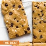 Peanut butter protein bars lined up with one pulled away from the others. A few chocolate chips are next to it.