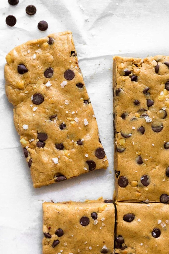 Peanut butter protein bars lined up with one pulled away from the others. A few chocolate chips are next to it.