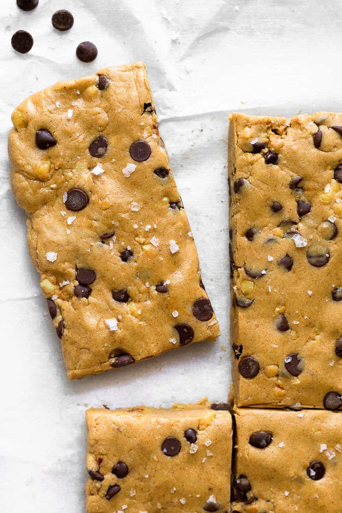 Peanut butter protein bars lined up with one pulled away from the others. A few chocolate chips are next to it.