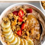 Protein yogurt bowl topped banana, granola, strawberries, peanut butter, and honey with a spoon in it.