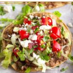 Beef tostada with beans, taco meat, lettuce, tomato, cheese, and cilantro on a baking sheet lined with parchment paper.