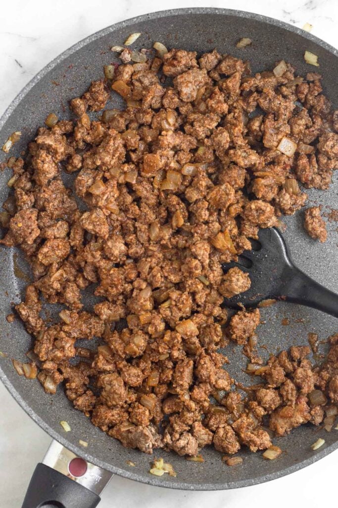Large skillet filled with seasoned ground beef and onions in it.
