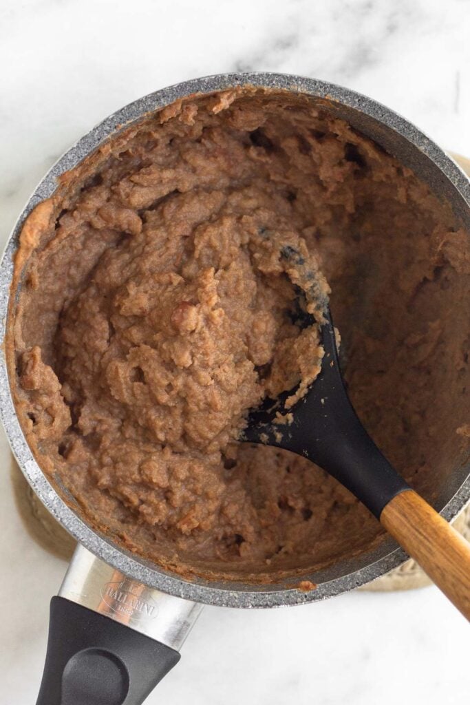 Sauce pan filled with warmed up refried beans in it.