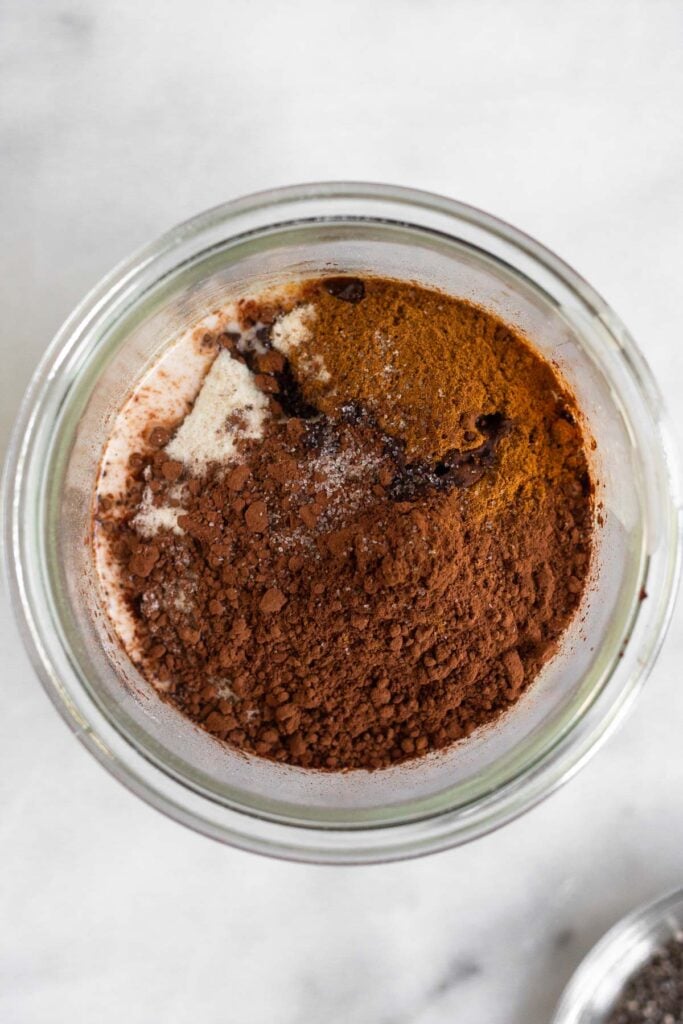 A jar with with coconut milk and sitting on the top of it is collagen, cocoa powder, cinnamon, and salt before it is mixed together.