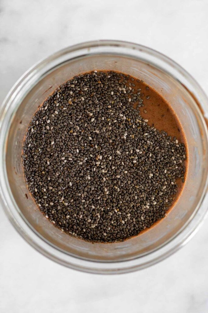 Liquid chocolate mixture with chia seeds sitting on top of it before it in mixed together in a jar.