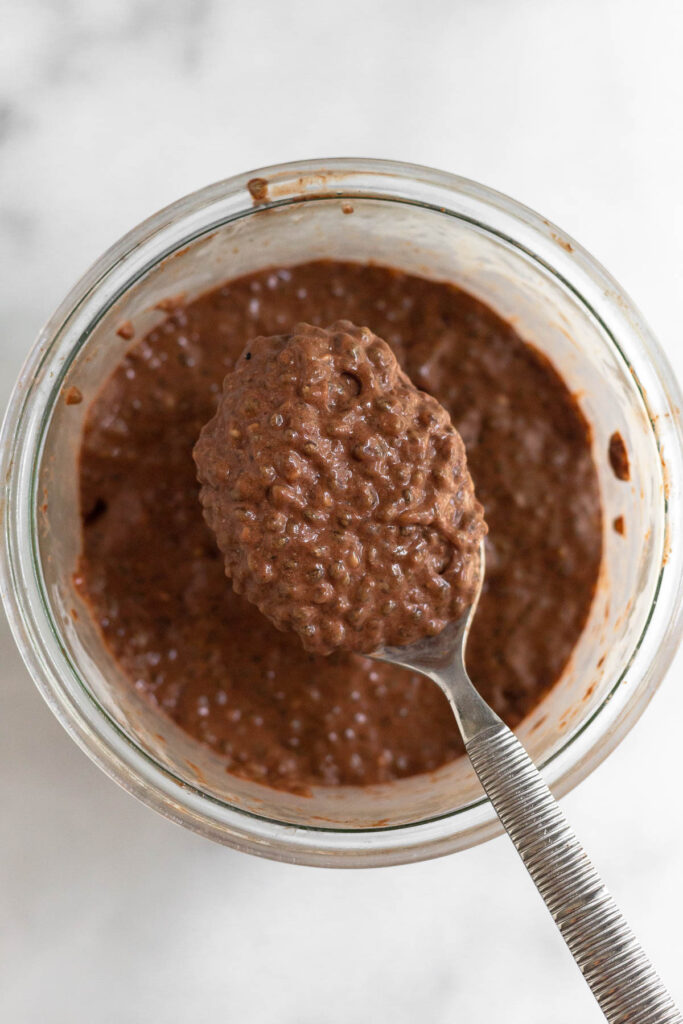 Chia chocolate pudding in a jar with a spoon overtop holding some.