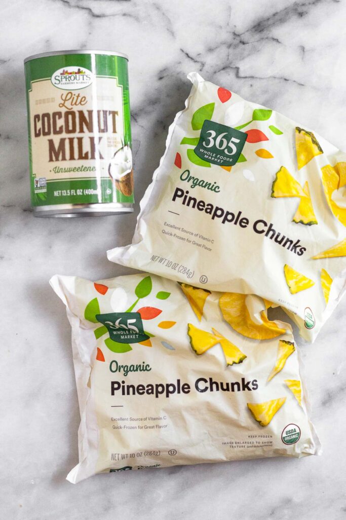White marble counter top with a can of lite coconut milk and two bags of frozen pineapple chunks.