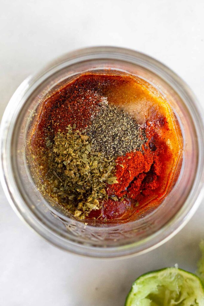 Glass jar filled with chipotles in adobo, lime juice, honey, and spices. Next to it is half a juiced lime.