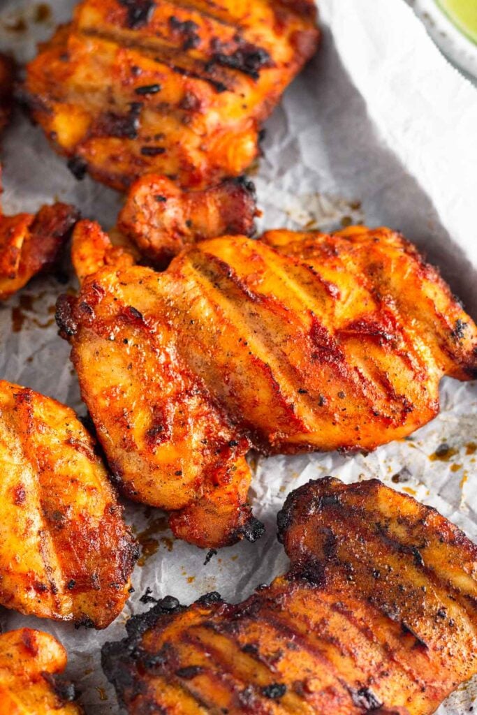 Close up of a grilled chipotle adobo chicken thighs surrounded by more grilled chicken thighs. They are on a baking sheet lined with parchment paper.