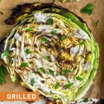 Close up a grilled cabbage steak on a baking sheet. It is garnished with ranch and fresh herbs.