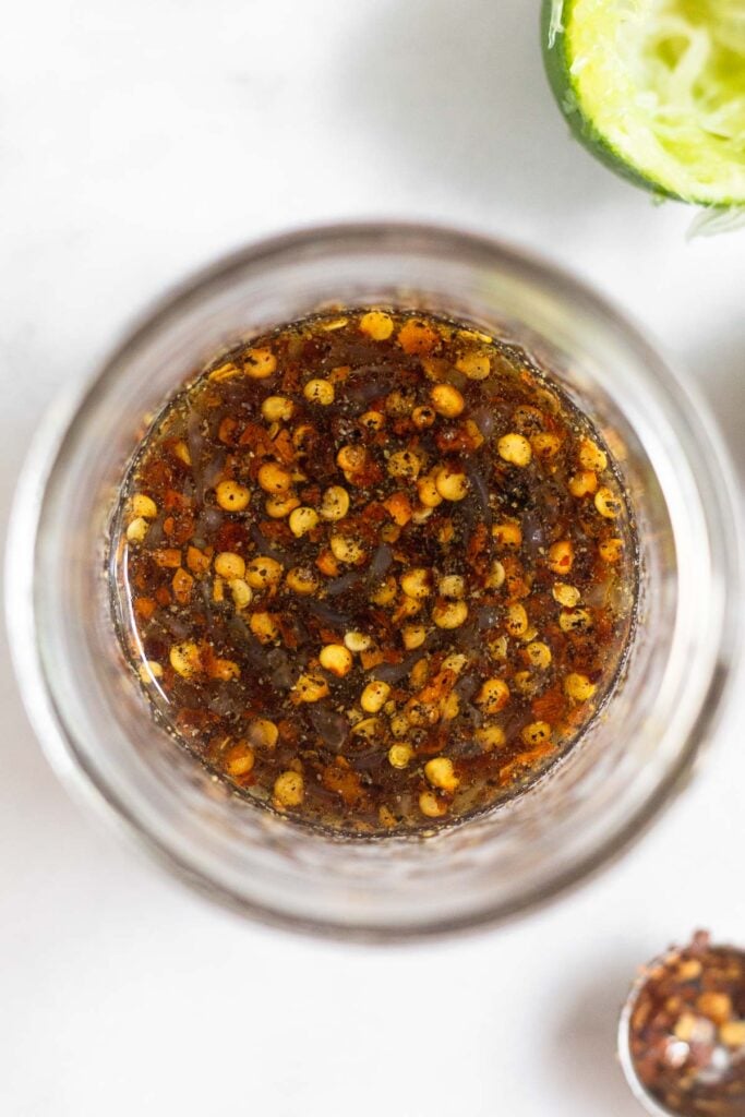 Small jar of stir fry sauce with red pepper flakes in it. Next to it is half a lime and teaspoon with some red pepper flakes still left in it.