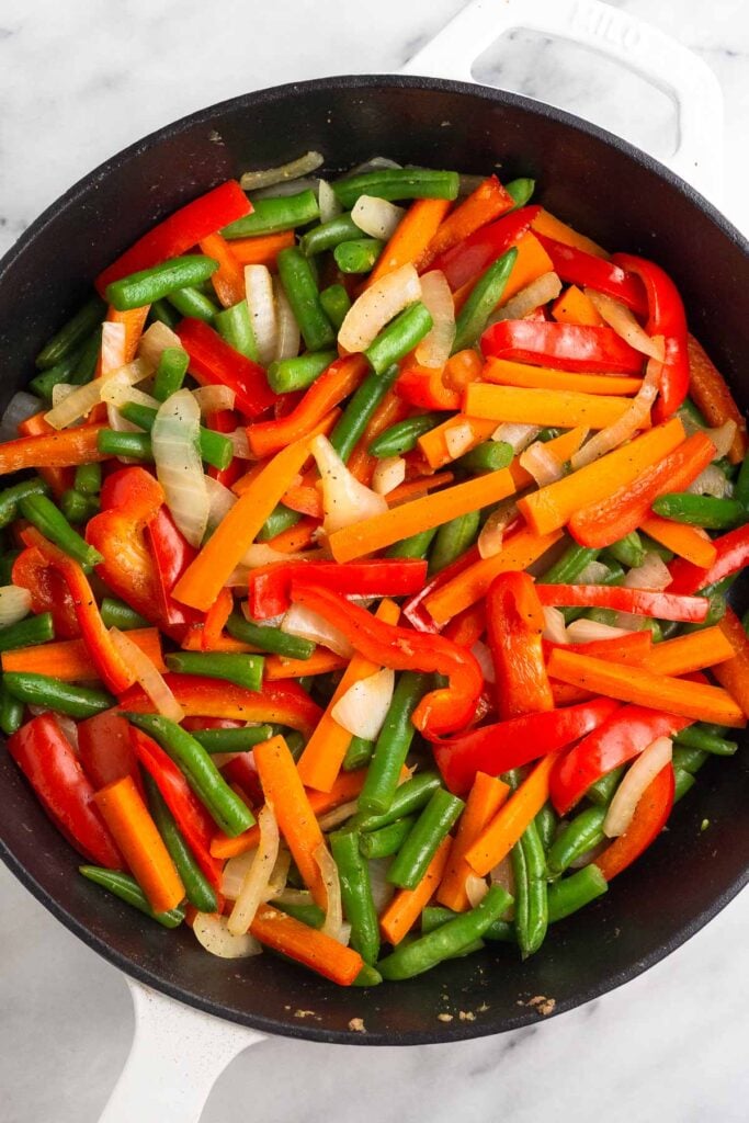 Cast iron skillet filled with sautéed peppers, onions, green beans, and carrots.