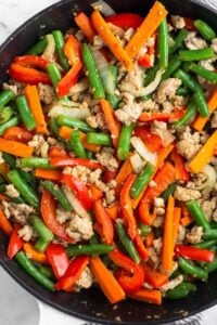 Cast iron skillet filled with ground turkey and sautéed peppers, onions, green beans, and carrots.