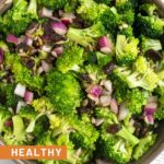 Healthy broccoli salad with raisins and sunflower seeds in a large bowl. The bowl is on a striped kitchen towel.