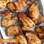 A bunch of pieces of grilled pickle brine chicken on a baking sheet garnished with lemon wedges and fresh dill.