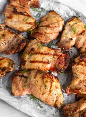 Grilled chicken that was marinated in pickle juice on a baking sheet. They are garnished with fresh dill.
