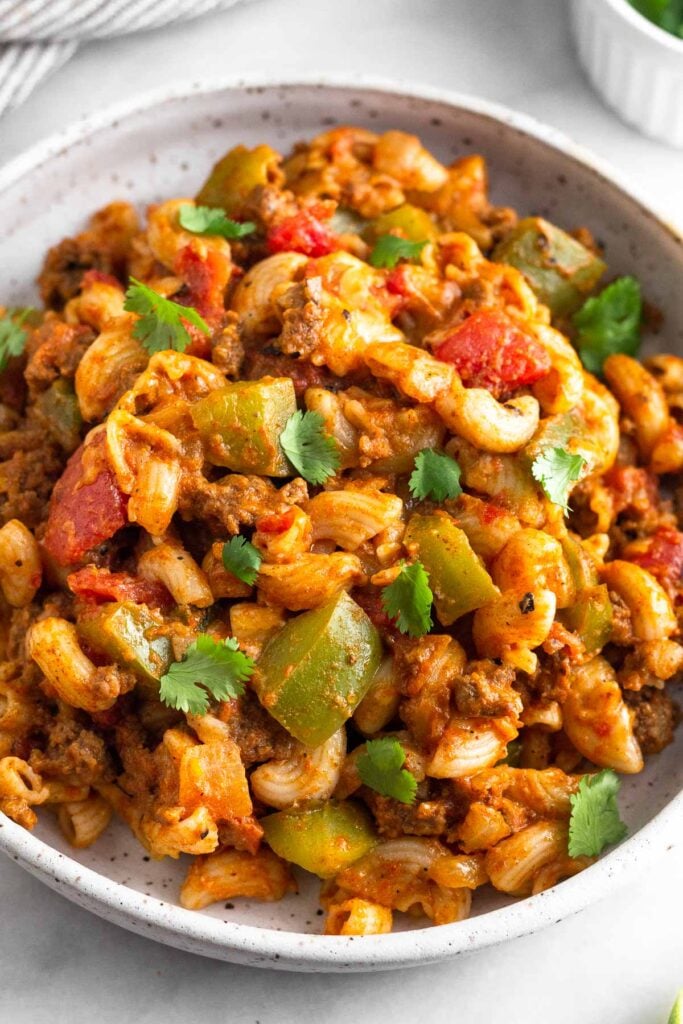 A plate of taco pasta topped with ground beef and veggies. It is topped with cilantro.
