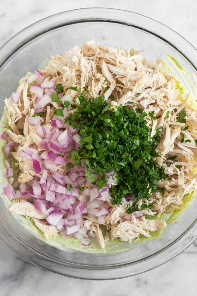 Large bowl with shredded chicken, diced red onion, and cilantro over top an avocado sauce.
