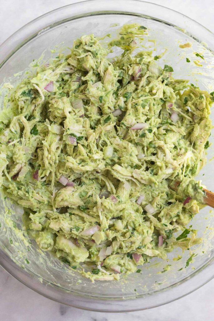Avocado chicken salad in a large glass bowl with a spatula in it.