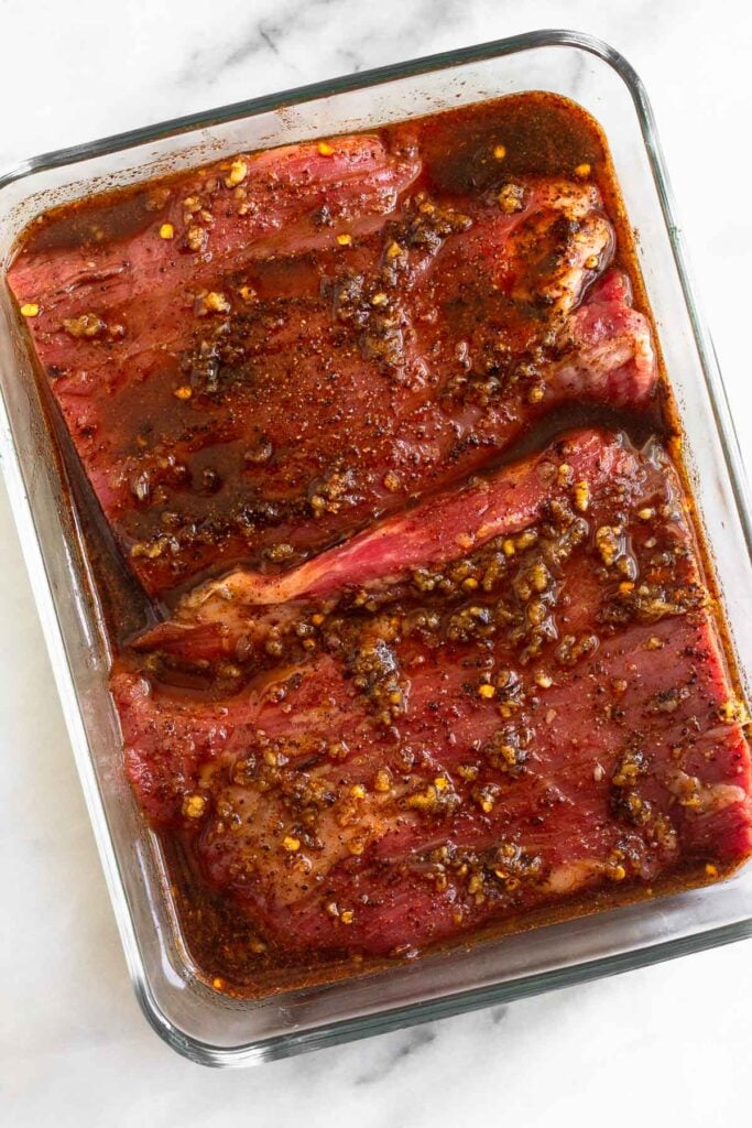 Glass dish with two pieces of steak sitting in a marinade in it.