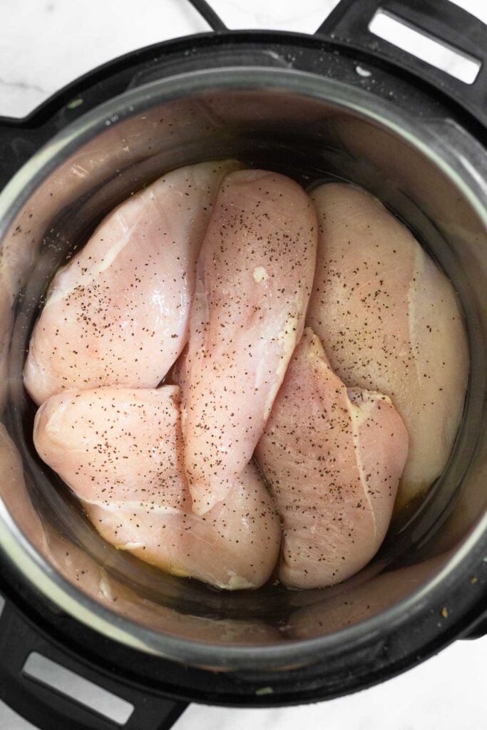 Instant pot filled with raw chicken breasts sprinkled with salt and pepper.