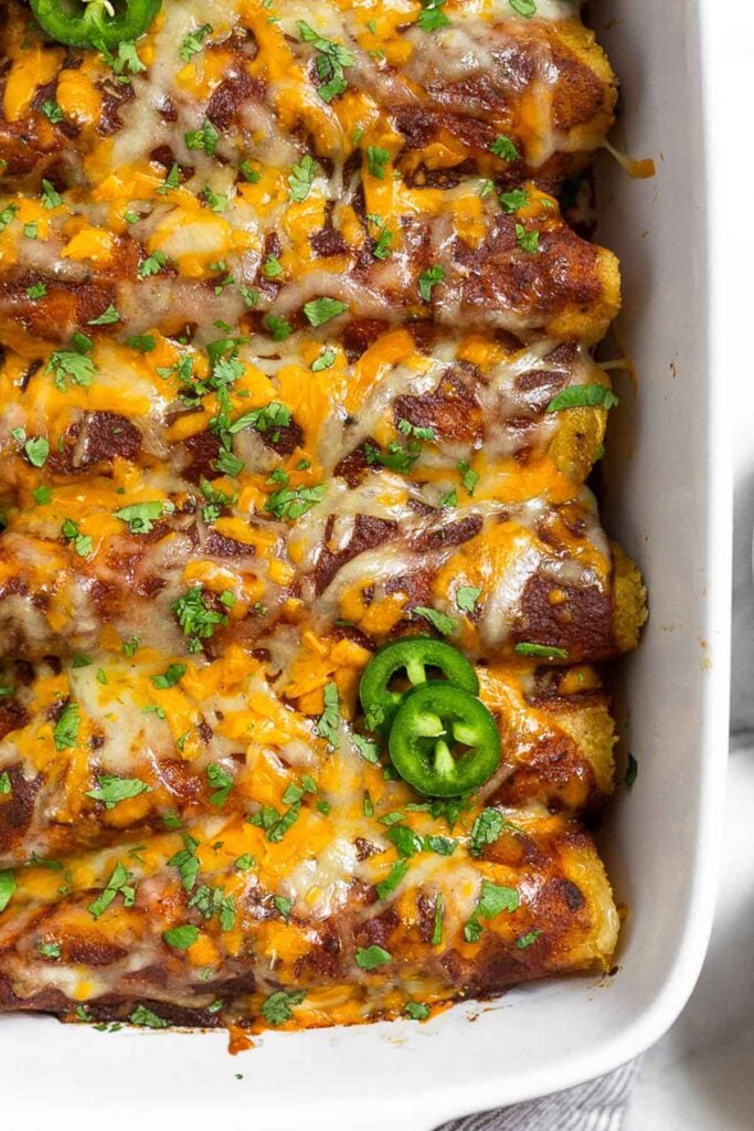 Shredded chicken enchiladas topped with melted cheese and sliced jalapeños in a large white baking dish.