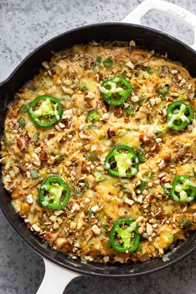 Overhead shot of a casserole in a large cast iron topped with cheese, crushed pretzels, and slices jalapeños.