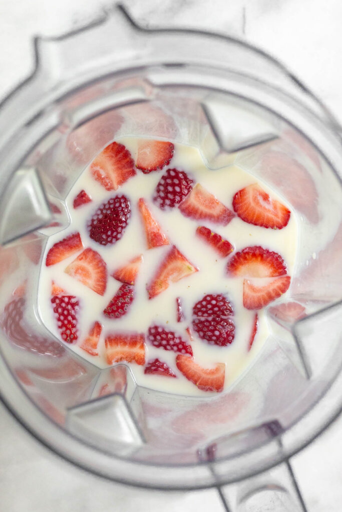 A blender with milk and diced strawberries in it.