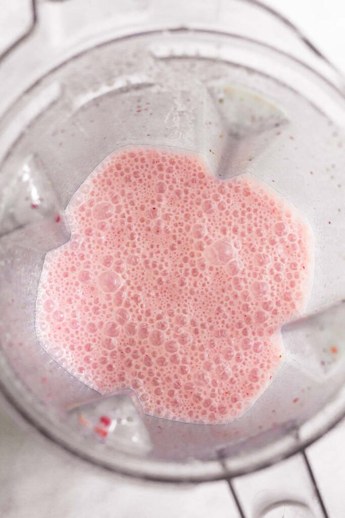 A blender with homemade strawberry milk in it.