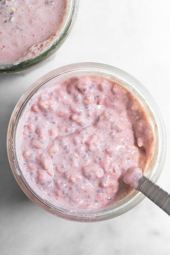 Overhead shot of two jars with strawberry overnight oats in them. One jar has a spoon in it.
