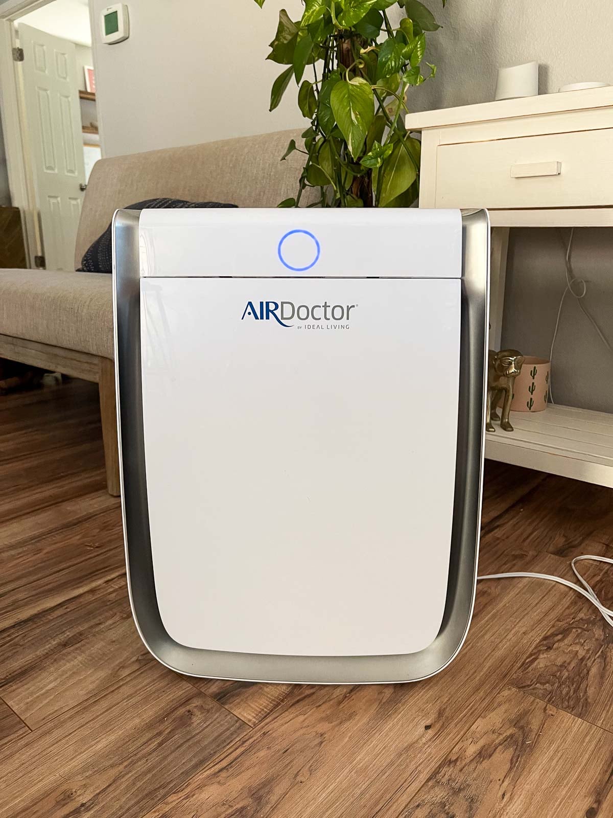 AirDoctor in a living room. Behind it is a small couch, a plant, and a white table.