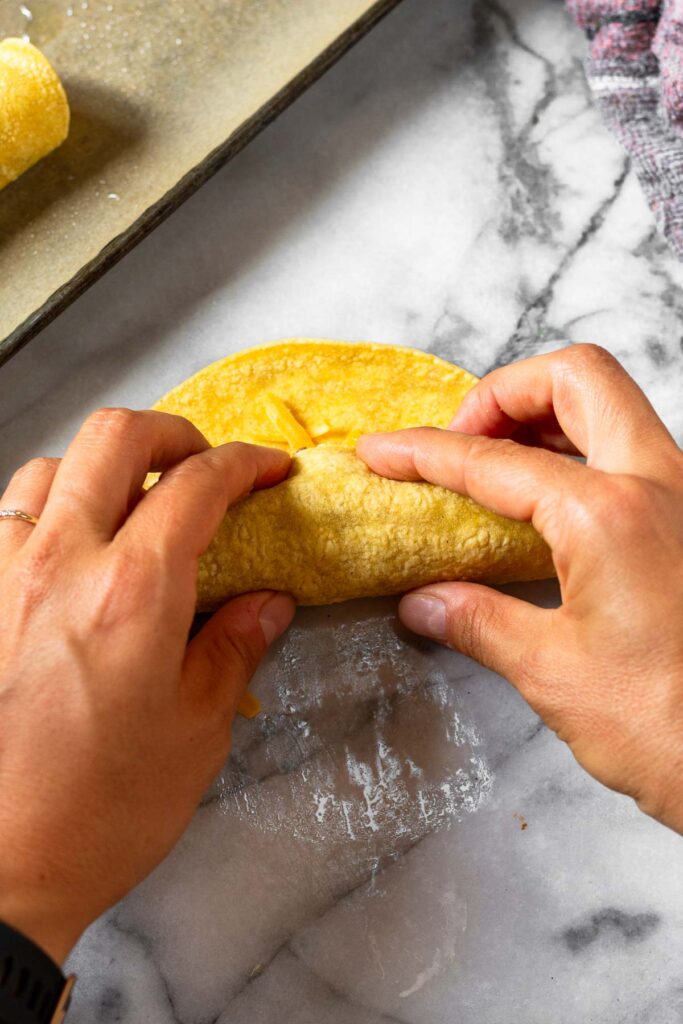 Corn tortilla filled with meat and cheese being rolled up.
