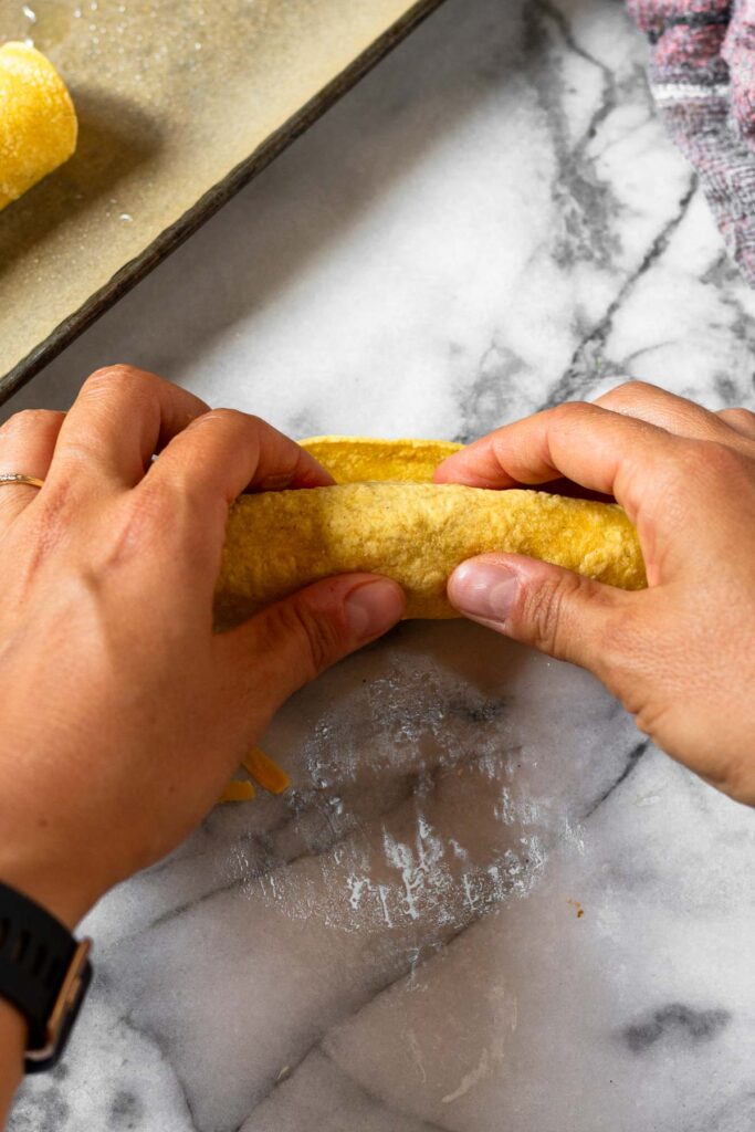 Overhead shot of a corn tortilla with meat and cheese in it being rolled up.