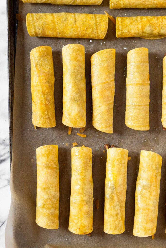 Baking sheet filled with taquitos before they are baked.