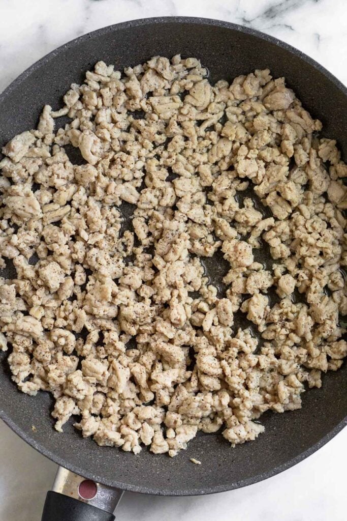 Large skillet filled with sautéed ground chicken.