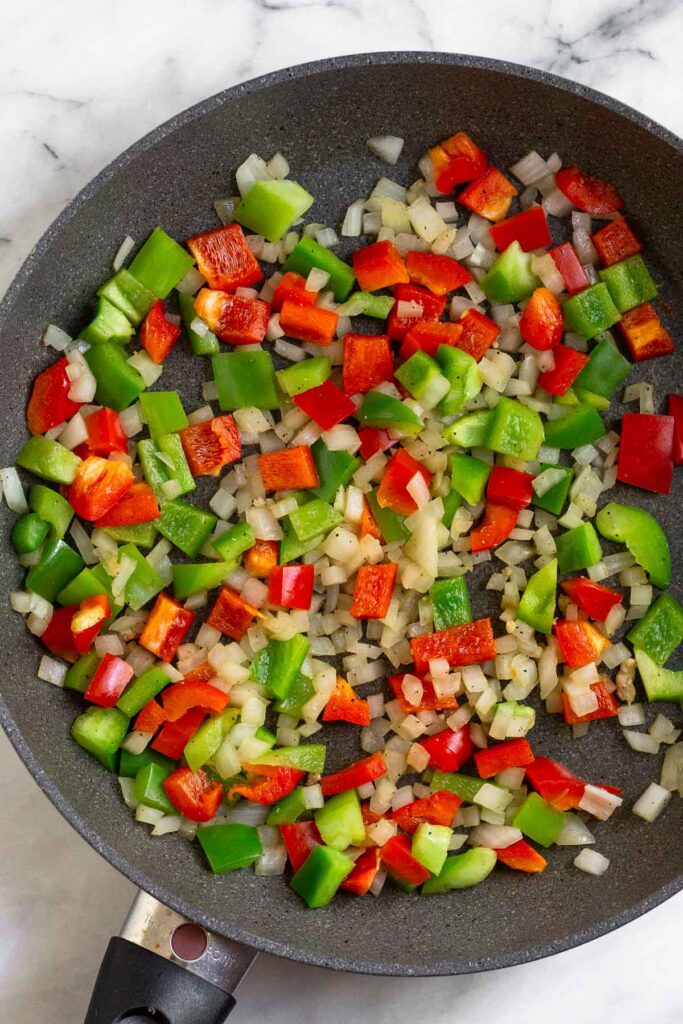 Large skillet filled with sautéed onions and peppers.