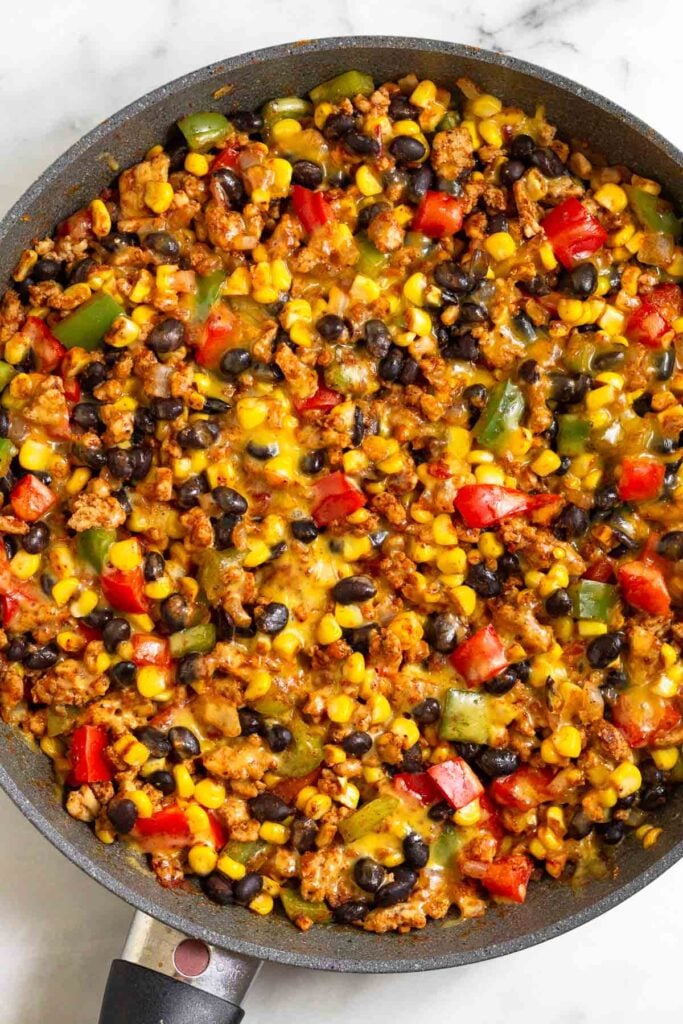 Large skillet filled with ground chicken, veggies, corn, and black beans topped with melted cheese.