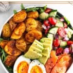 Protein breakfast bowl recipe with greens, roasted potatoes, tomato and cucumber salad, smoked salmon, hard boiled egg, and avocado topped with everything but the bagel seasoning.