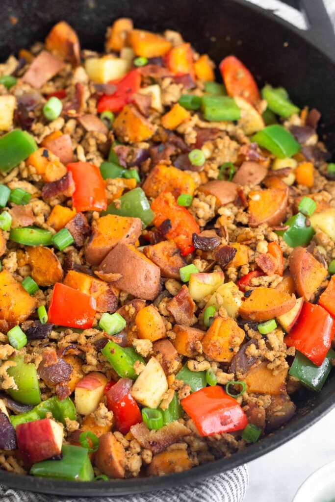 Protein breakfast hash recipe with ground chicken, sweet potatoes, bacon, and veggies in a large cast iron skillet.