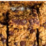 A baking dish of oatmeal chocolate chip bars in it with the middle one slightly resting on the one in front of it so you can see the inside of it.