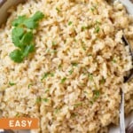 Overhead shot of cheesy rice in a large white bowl garnished with cilantro. There is a spoon in the bowl and the bowl is on a striped kitchen towel.
